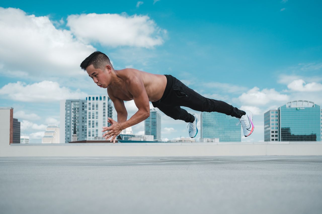 A muscular man performing a stretch on a rooftop with Orlando skyline in the background.
