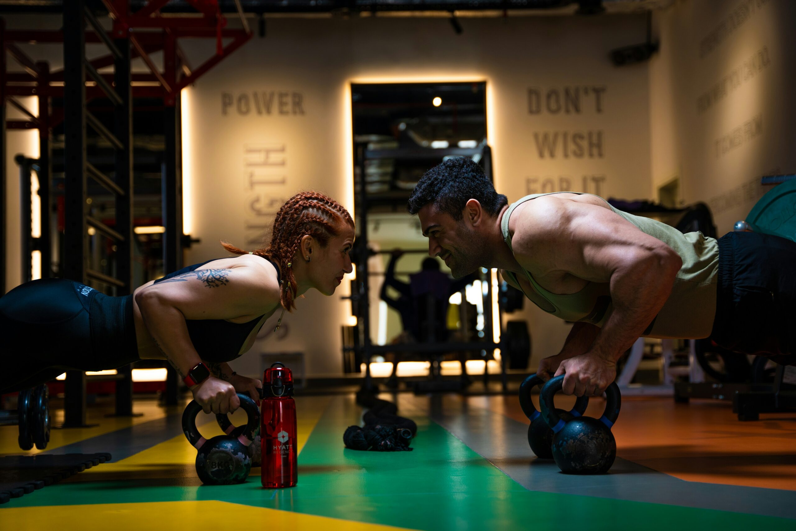 Two people performing push-ups with kettlebells in a gym